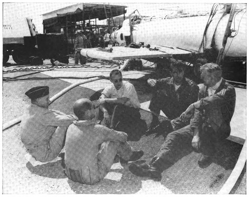 Several men sitting in a circle on the tarmac next to a plane