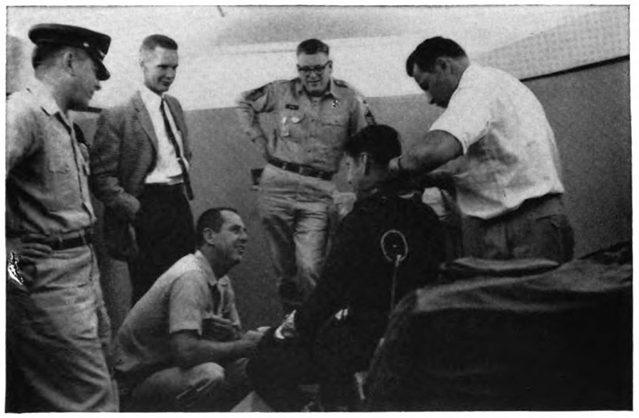 Men standing and sitting around a seated man