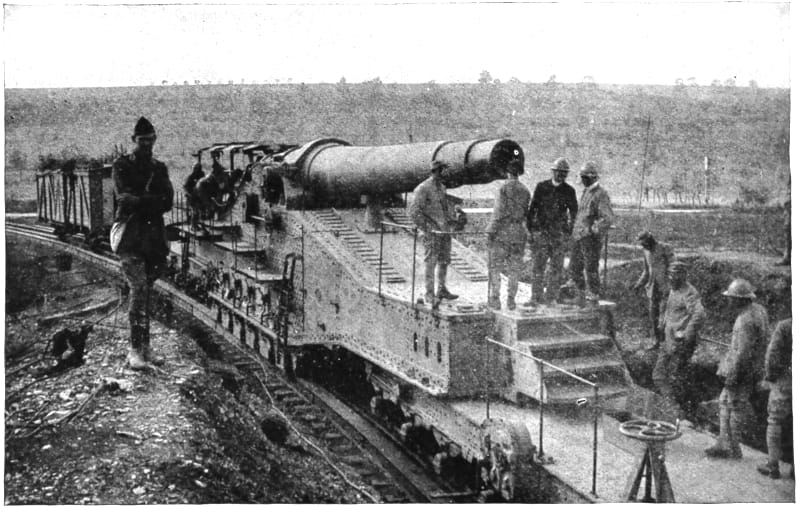 Uniformed men standing near a gun on a rail car on rails.