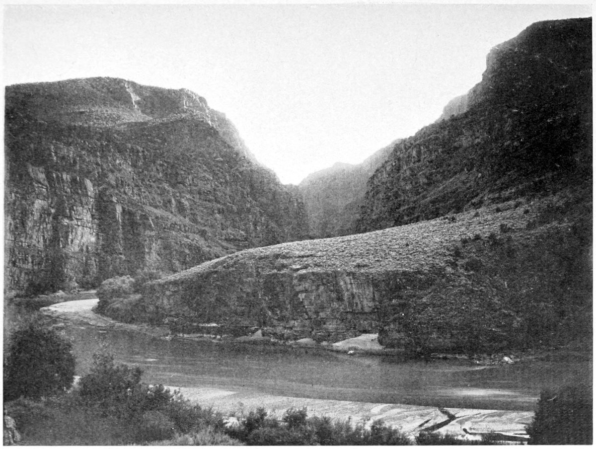 A placid river spans the lower third of the photo. Land slopes gently upward to the right; a vertical canyon wall is on the left.