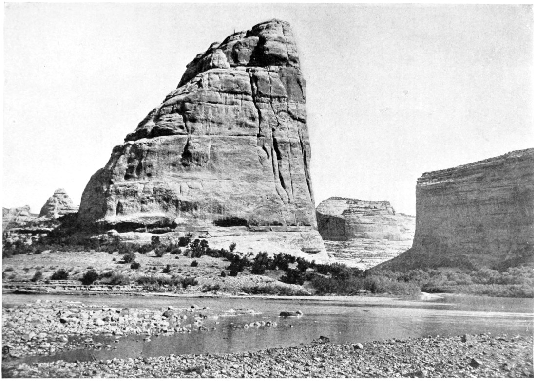 View of a canyon wall that is vertical on the river side, eroded into a slope on the other.