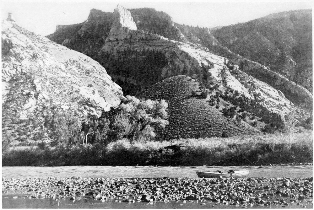 At the bottom of the photo, one boat sits on a wide rocky beach that spans the width. Beyond the beach, rocky hills, some with trees or scrub brush, rise gently to the horizon, at the top of the image.
