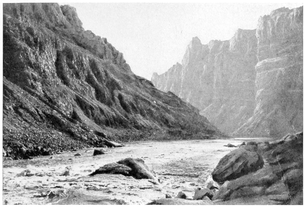 Water rushes around rocks in the middle of the river. A sloped canyon wall is on the left, a more vertical wall is on the right.