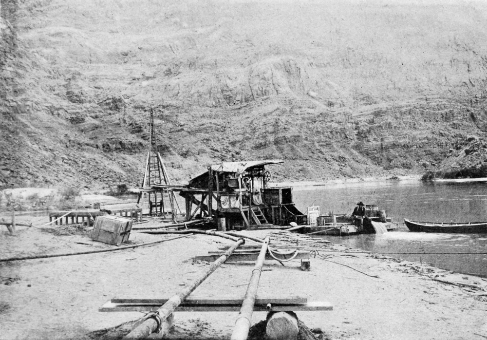 A dredge is operating at the shoreline; pipes and equipment are scattered in the vicinity along the shore.