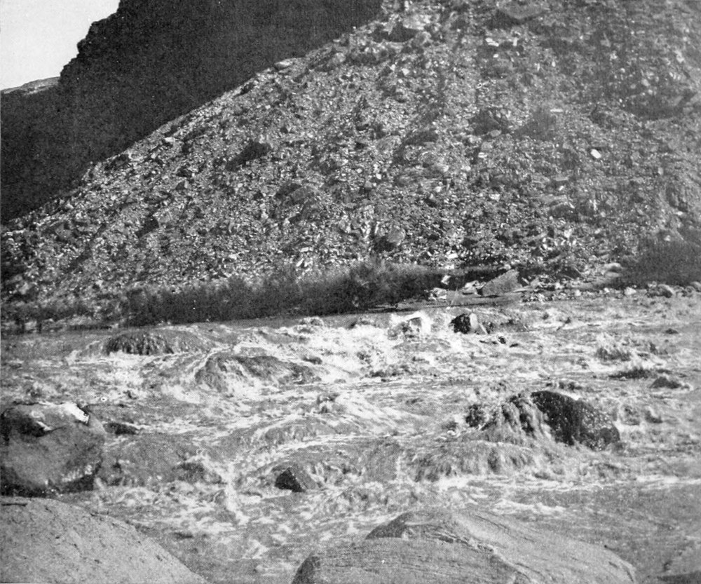 Water churns through rocky rapids; a boat is barely visible amid the foamy water.