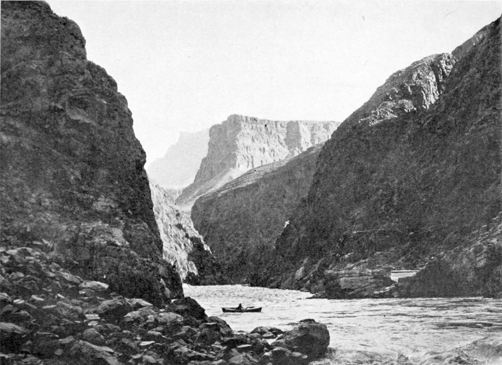 A boat is in the running river. Sunlight and shadows play on the canyon walls.