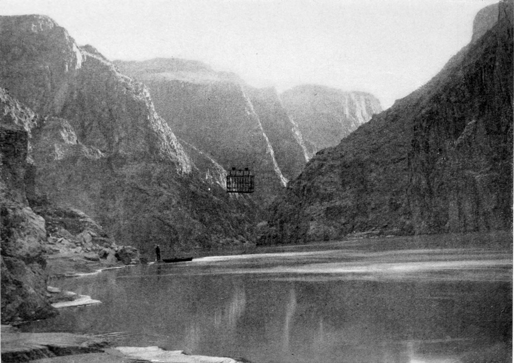 A metal cage runs on wheels over a cable that crosses the river between canyon walls. Two men at the shoreline watch the tram from below.