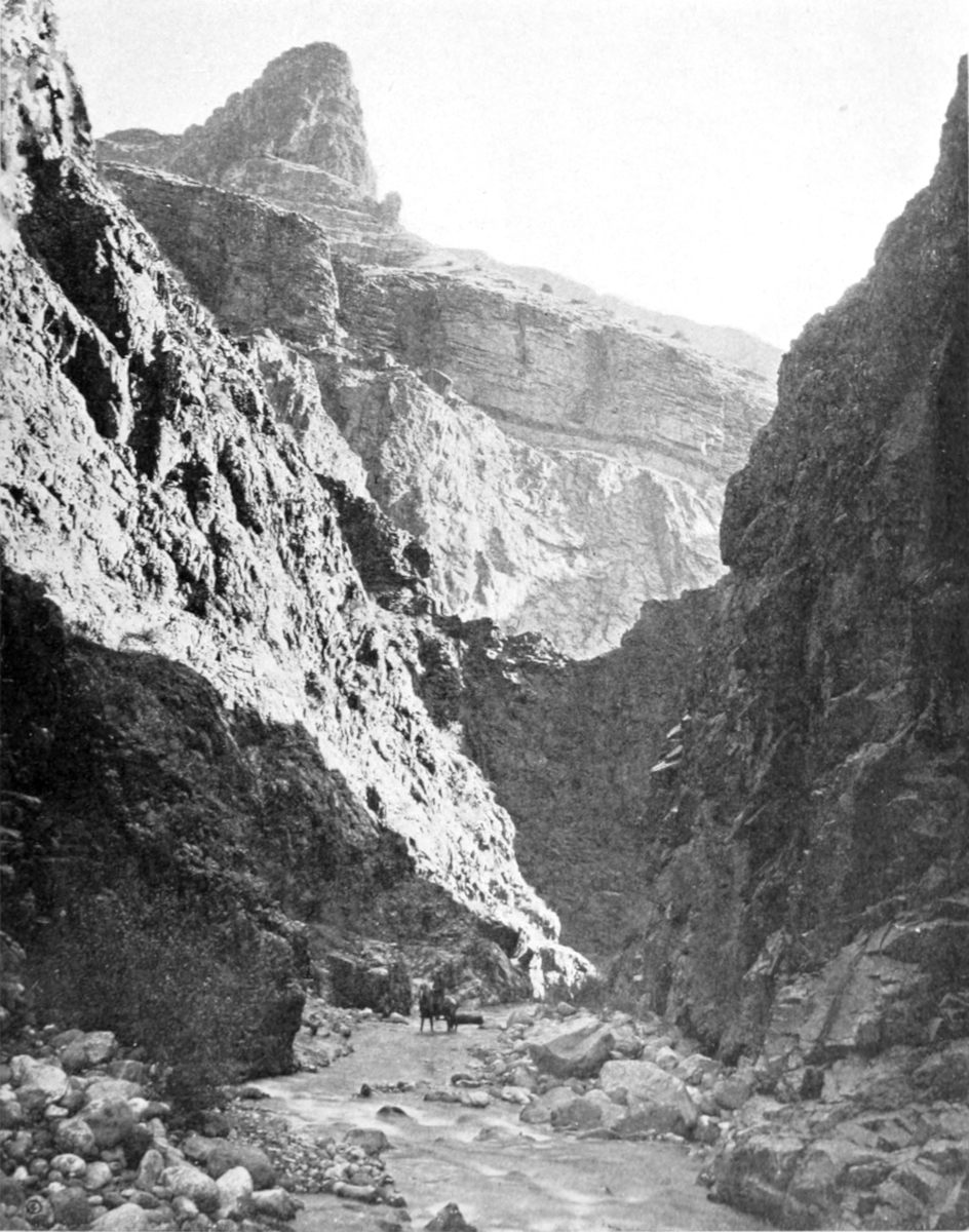 Close canyon walls confine a small creek full of rocks.