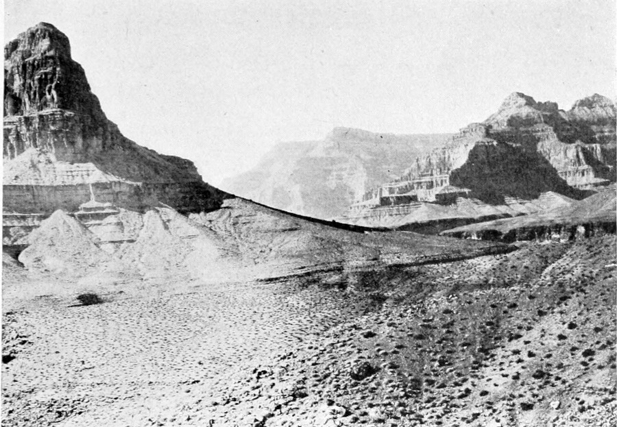 Canyon peaks rise from a barren plateau of eroded stone and small rocks.