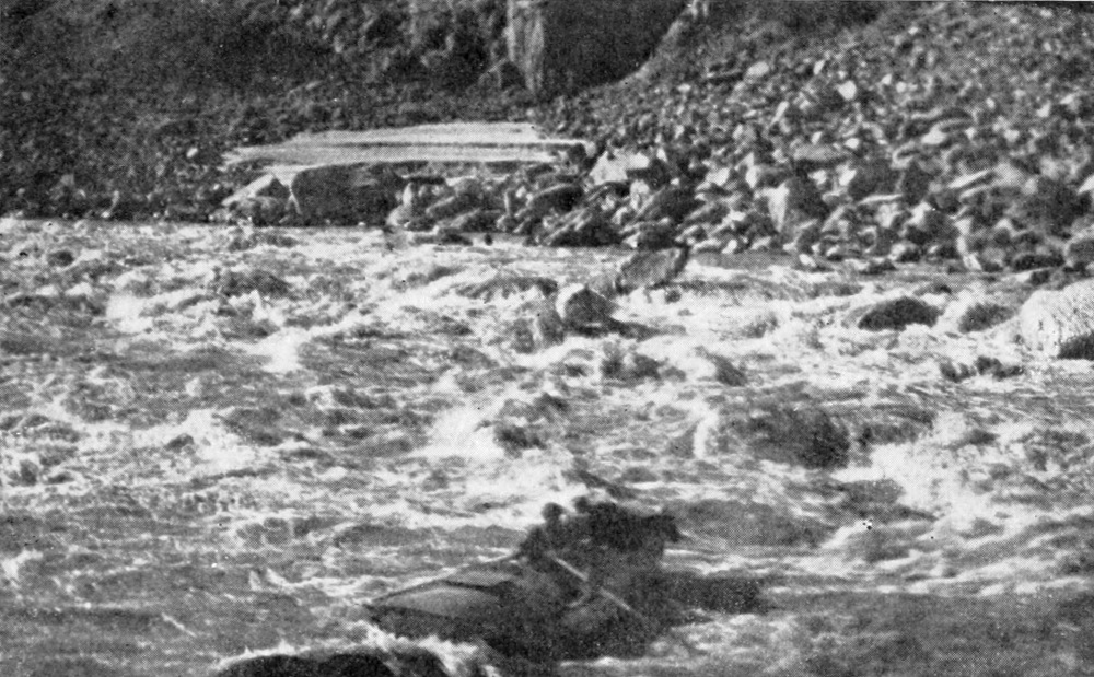 A boat with one man in the cockpit and another riding on the prow rides through a the rapids.