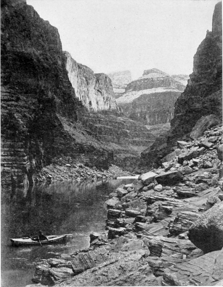 One boat is in the calm water at the lower portion of the photo. High canyon walls rise from the foreground to the distant background.
