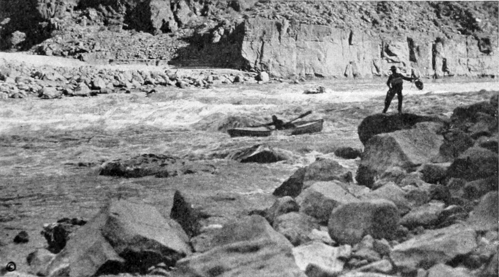 This is a wider view of the above photo taken a moment later. The man in the boat has progressed towards a rock. Standing on a rock, another man holds a life preserver on a line, ready to throw it to the boater, if needed.