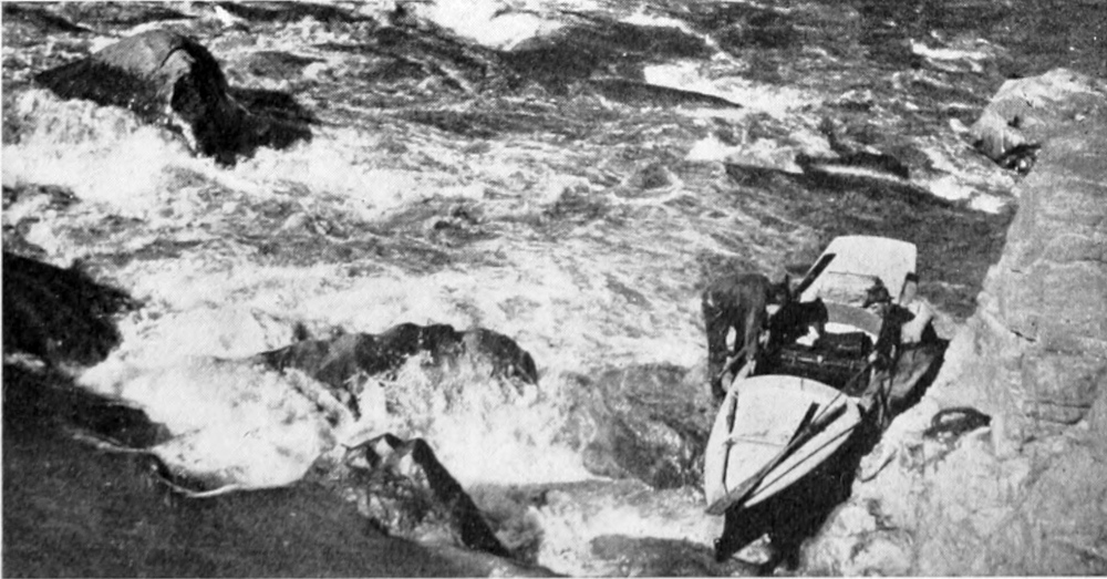 Two men stand on rocks in the river on either side of a boat, holding it against the flow of the water.
