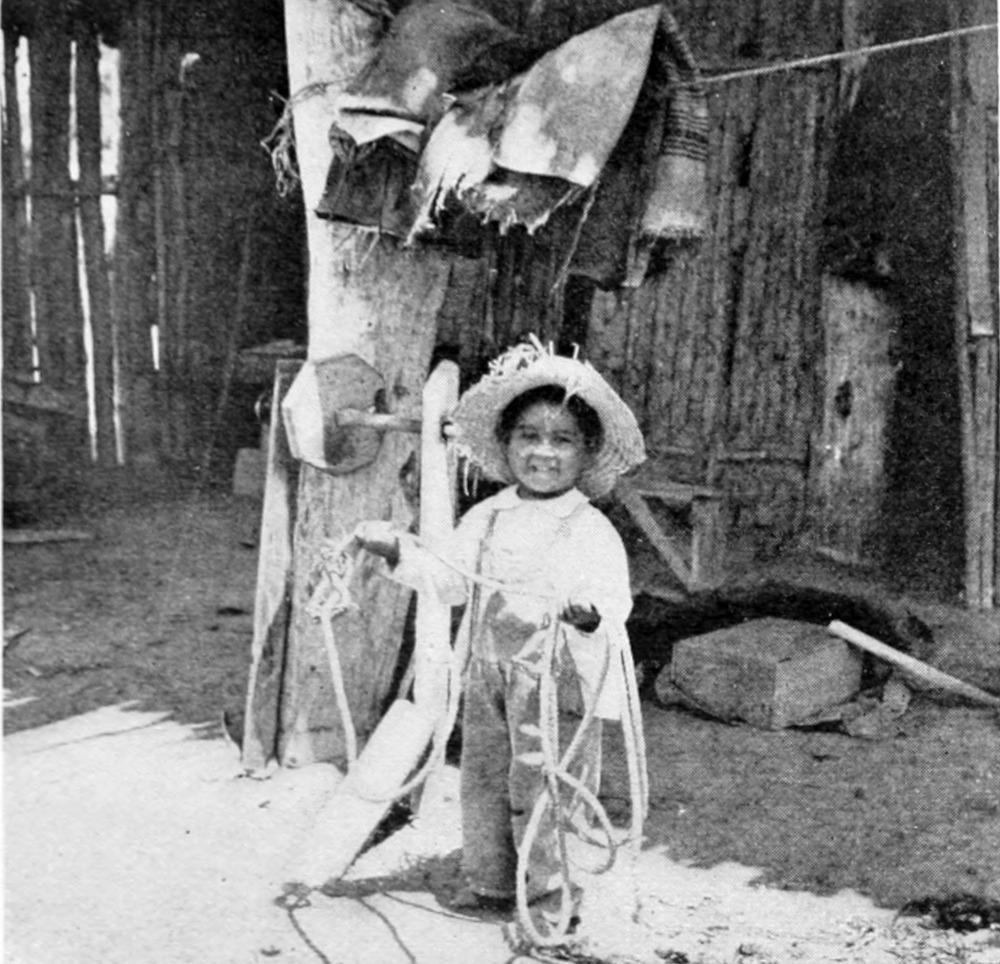 A child wearing a sombrero and carrying a lasso smiles at the photographer.