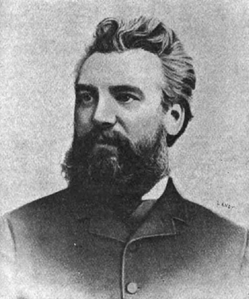 A photograph of a bearded man with swept-back hair in 19th-century dress — consistent with portraits of Alexander Graham Bell, inventor of the telephone.